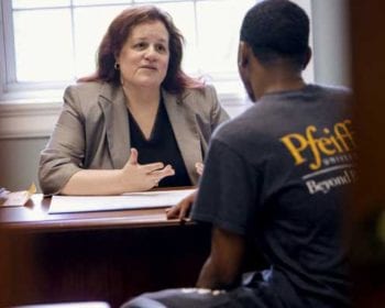 woman talking to male student at desk
