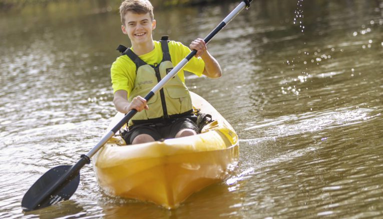 Male student kayaking on lake