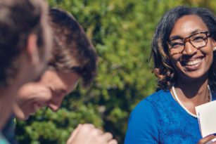 Three students sitting outside talking and smiling
