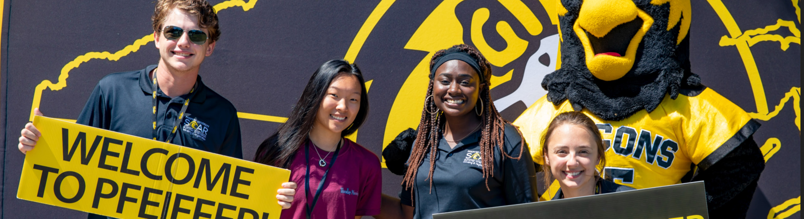 Group of students with Pfeiffer mascot holding welcome sign